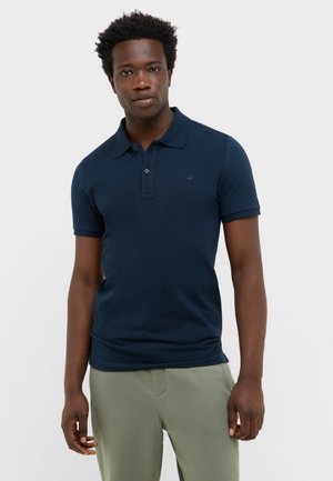 Granatowa koszulka polo z kołnierzykiem i krótkimi rękawami, z delikatnym logo na klatce piersiowej oraz teksturowanym materiałem. Spodnie są w kolorze oliwkowym.