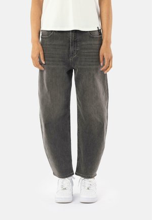 Black denim jeans with a relaxed fit; features five pockets and visible stitching; paired with white sneakers and a short white top.