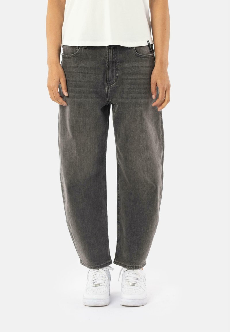 Jeans in denim nero con una vestibilità rilassata; presentano cinque tasche e cuciture visibili; abbinati a sneakers bianche e a un top corto bianco.