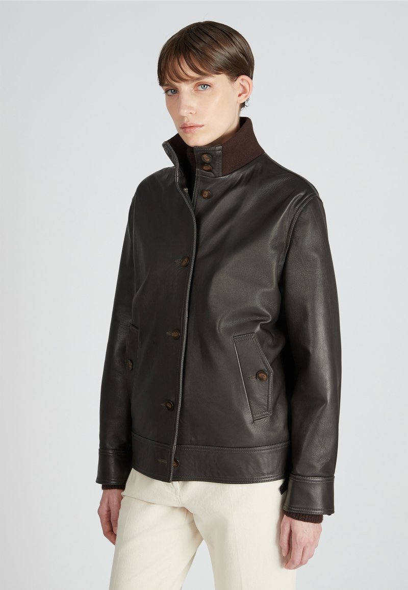Braune Lederjacke mit hohem Kragen, Knopfschluss und Taschen auf der Vorderseite. Glatte Textur, lässiges Design und kontrastierender dunkelbrauner Kragen.