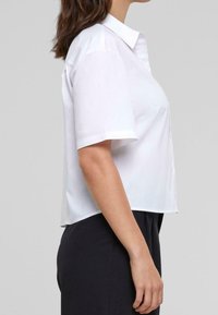 White short-sleeve collared shirt, textured fabric, cropped design, front button closure, with a smooth finish and straight hem.