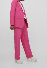 Ljusröd skräddarsydd kostym med en enfärgad kavaj och raka byxor, kombinerad med klumpiga krämfärgade plattformsskor.