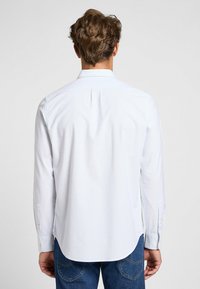 Camisa de manga larga azul claro con cuello abotonado, pliegue en la parte trasera y dobladillo redondeado. Confeccionada con tejido suave y ligero.