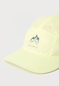 Ανοιχτό κίτρινο καπέλο από αέρινο ύφασμα, με πλέγμα πάνελ, καμπυλωτή γείσο και λογότυπο βουνού σε πράσινο χρώμα.