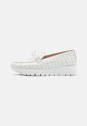 Chaussure blanche à enfiler avec un motif de grille texturé, bout arrondi et semelle en wedge blanche. Présente un détail décoratif de nœud à l'avant.
