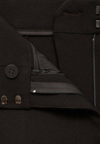Black fabric featuring a button and zipper closure, with a textured lining and visible stitching details. Multiple pockets included.