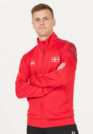 Rød sportsjakke med høj krave, fuld lynlås, logo på brystet og struktureret mønster på skuldrene. Fremstillet af glat, let materiale.
