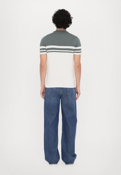 Pikétröja i grått och vitt, med ränder på ärmarna, i kombination med löst sittande blå jeans. Bakifrån visas.