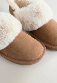 Brown suede slippers with thick cream-colored faux fur lining and trim, designed for indoor comfort and warmth.