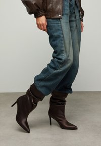 Bruine satijnen enkellaarsjes met hoge hak, een nonchalant ontwerp, puntige neus en taps toelopende hak, gecombineerd met losvallende blauwe spijkerbroeken.