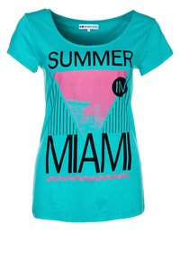 Camiseta de algodón turquesa con un gráfico triangular rosa que incluye el texto "VERANO EN MIAMI" en negro y un patrón geométrico en la parte inferior.