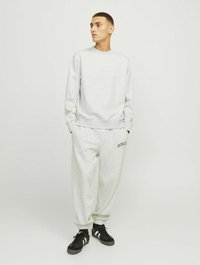 Felpa grigia con collo a giro e polsini a coste, abbinata a pantaloni jogger grigi con dettaglio del logo. Sneakers nere completano l'outfit.