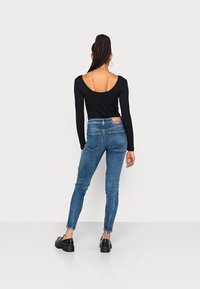Top negro de manga larga con un escote profundo en la espalda, combinado con unos vaqueros ajustados de denim azul. Textura suave; los vaqueros cuentan con una etiqueta y bolsillos traseros.