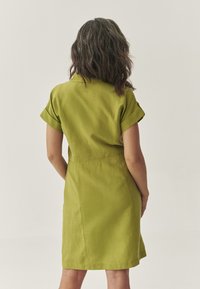 Abito a maniche corte con colletto in lino verde vibrante. Vestibilità dettagliata con risvolti, che mostra una texture liscia e cuciture pulite sul retro.