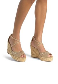 Sandales compensées beiges avec une plateforme en paille texturée, bout ouvert, design à brides croisées et ornées de strass sur le dessus.