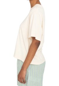 Lichtbeige katoenen t-shirt met korte mouwen en een losse pasvorm, gecombineerd met groen-witte gestreepte broek. Eenvoudig ontwerp, minimale details.