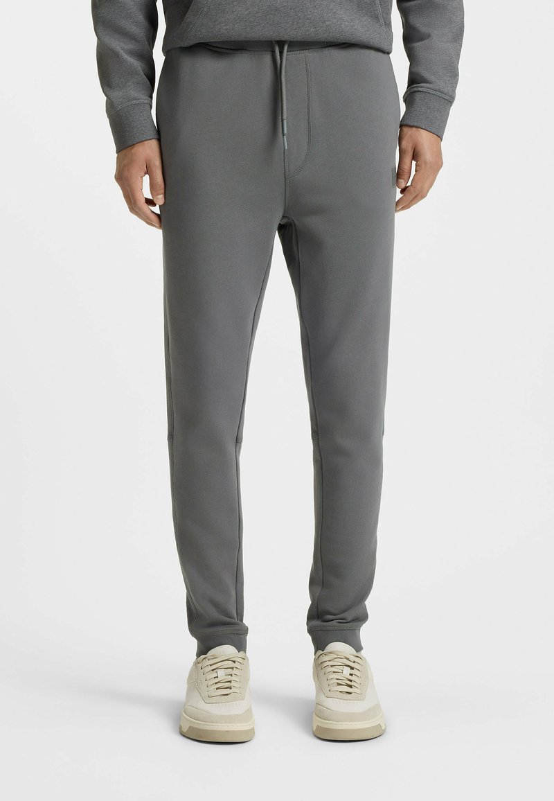 Grå sweatpants lavet af blødt stof, med en elastisk talje med snørre, mellemlange ben og sidelommer.