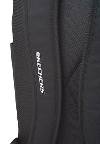 Mochila negra con un diseño de malla texturizada, con correas ajustables y un prominente logo blanco de "SKECHERS" en un lado.