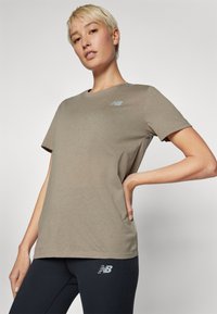 T-shirt vert olive à manches courtes en matière douce, avec un logo bleu clair sur la poitrine. Associé à des leggings noirs.