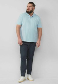 Helles blaues Polohemd mit Kragen und kurzen Ärmeln, kombiniert mit dunkelblauen Hosen und weißen Sneakers. Einfaches Design und weicher Stoff.