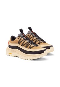 Beige ja mustad spordijalatsid tekstuurse viimistlusega, millel on paks tall ja kontrastsed paelad, samuti Gore-Texi bränding külje peal.