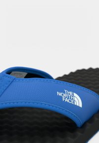 Μπλε σανδάλι με ιμάντα και υφή μαύρης σόλας, με το λευκό λογότυπο "The North Face" στο πλάι του ιμάντα.