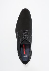 Chaussure habillée noire en suede avec des coutures claires, bout rond et design à lacets. L'intérieur présente une étiquette de marque avec des accents rouges.