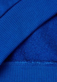 Niebieska tkanina o fakturowanym splocie i gładkich, żebrowanych krawędziach. Widoczne szwy na dole, wskazujące na warstwową konstrukcję tekstyliów.