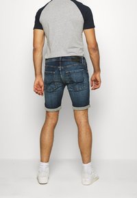 Shorts de mezclilla con dobladillos enrollados, lavado azul oscuro, cinco bolsillos y una parche negro en la cintura trasera. Combínalos con una camiseta raglán gris y azul marino.