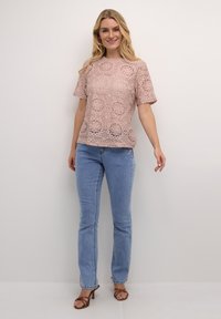 Top in pizzo rosa tenue con motivi floreali, maniche corte e scollatura rotonda. Abbinato a jeans azzurri chiari e sandali con tacco marroni.