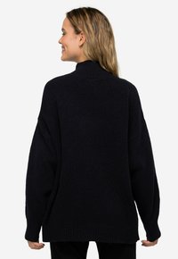 Übergröße schwarzer Pullover mit hohem Kragen, gerippten Bündchen und Saum. Weicher Stoff und lockere Passform für besonderen Komfort.