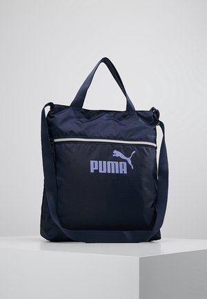 Navy blue Puma tote bag with front zipper pocket, two short handles, and one adjustable long shoulder strap on a white pedestal.
