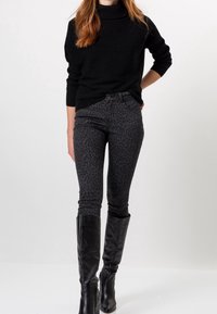 Černý pletený svetr s vysokým límcem, zkombinovaný s tmavě šedými skinny džínami s leopardím potiskem a černými koženými botami po kolena.