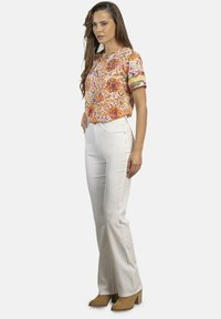 Blusa ligera y estampada en tonos naranja, rosa y blanco; combinada con pantalones blancos ajustados. Botines marrones hasta el tobillo completan el conjunto.