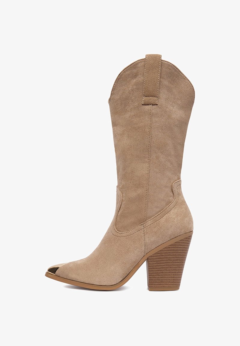 Bézs színű, térdig érő velúr csizma hegyes orral, bevágott szegéllyel és rétegezett sarokkal, amelyet vízszintes csíkok díszítenek a textúráért.