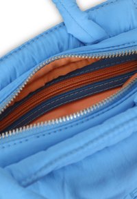 Kék szövet táska textúrált felülettel, élénk narancssárga belső térrel és több, kontrasztos színű, cipzáras rekesszel.