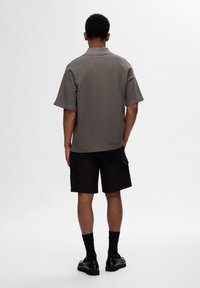 Polo gris à manches courtes avec un tissu texturé, associé à un short cargo noir avec des poches latérales. Les chaussures sont des mocassins noirs portés avec des chaussettes.