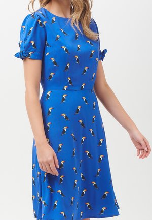 Blå kortærmet kjole med puffede ærmer og sløjfedetaljer, med et mønster af små farverige tukaner.