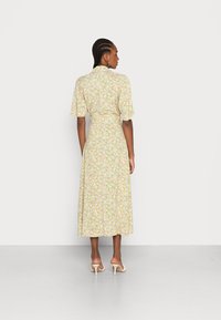 Vestido midi floral em amarelo claro com mangas curtas, cintura ajustada e bainha leve. Apresenta um padrão delicado com detalhes em rosa e verde.