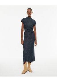 Top de punto acanalado azul oscuro con mangas cortas, combinado con una falda larga hasta los tobillos a juego. Llevado con botas de cowboy beige.