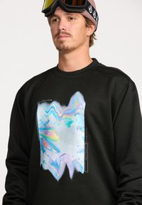 Sweatshirt noir avec un design graphique texturé et coloré présentant des motifs ondulés en bleu, rose et accents argentés. Le modèle porte des lunettes de ski.