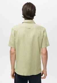 Camisa de manga corta, de color verde claro y hecha de lino. Presenta un cuello abotonado y una yugo trasero recto. Acabado texturizado sutil.