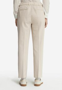Beżowe spodnie z lekkiego materiału, o dopasowanym kroju, z elastyczną talią i kieszeniami z tyłu. Połączone z jasnym obuwiem.