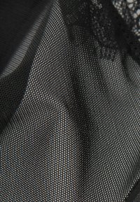 Tissu en maille noire avec une texture fine et en grille, comportant de délicates accentuations en dentelle le long d'un bord. Matériau doux et léger avec un léger éclat.