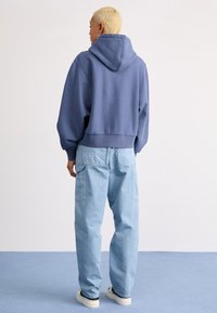 Sweatshirt à capuche en tissu bleu doux, à coupe courte. Associé à un pantalon cargo ample bleu clair avec poches. Baskets blanches.