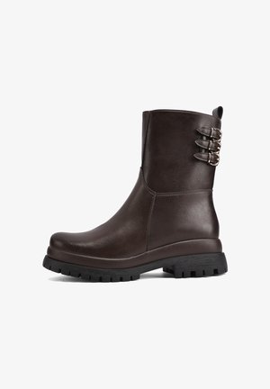 Stivale alla caviglia in pelle marrone con punta arrotondata, superficie testurizzata e doppie fibbie sui lati. Suola in gomma nera spessa per una buona aderenza.