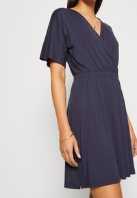 Niebieska sukienka mini z miękkiego materiału, z dekoltem w serek, krótkim rękawem oraz elastyczną talią, która podkreśla sylwetkę.