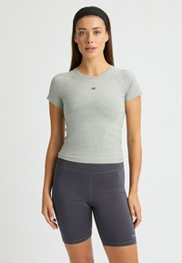 Camiseta gris ajustada de manga corta, fabricada con un tejido texturizado, combinada con pantalones cortos de ciclismo oscuros de talle alto que cuentan con bolsillos laterales y costuras planas.