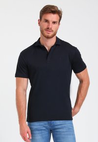 Temno modra polo majica s kratkimi rokavi, ovratnikom in dvobutonskim zapenjanjem. Narejena je iz gladkega materiala in ima majhen logo na prsih.