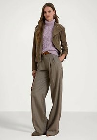 Γυναίκα που φοράει καφέ σουέτ μπουφάν πάνω από λιλά τζάκετ με ζιβάγκο, γκρι παντελόνι με φαρδιά πόδια, καφέ ζώνη, κρατώντας καφέ τσάντα.